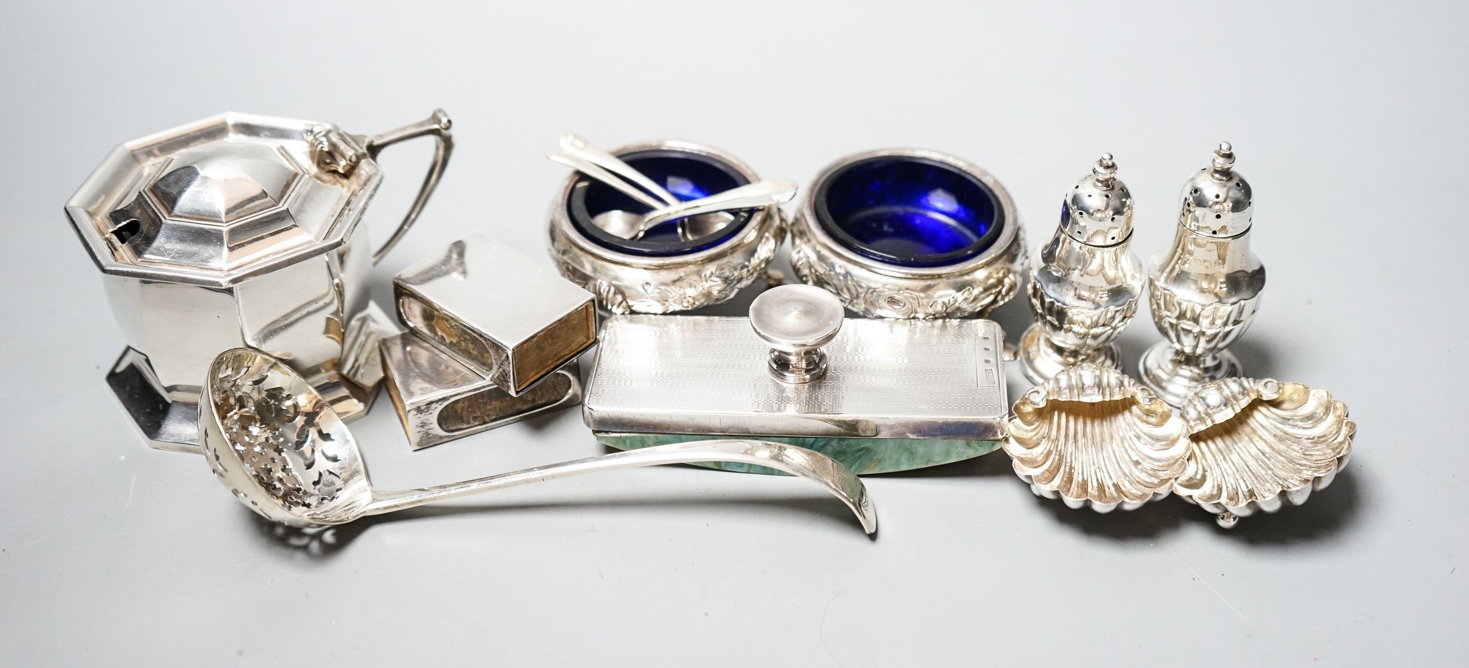 Small silver including a George V silver octagonal mustard, two Victorian bun salts, two shell salts, George III sifter spoon, two condiments, a blotter and two match box sleeves.